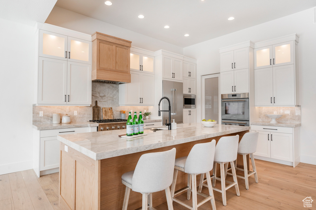 Kitchen featuring light hardwood / wood-style flooring, stainless steel appliances, a center island with sink, and backsplash