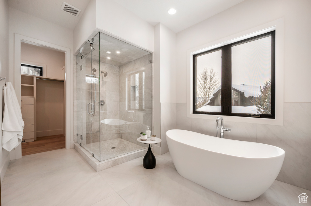 Bathroom featuring tile floors, separate shower and tub, a wealth of natural light, and tile walls