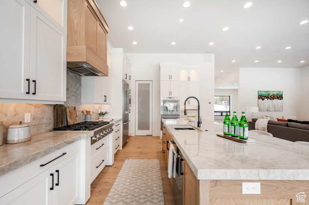 Kitchen featuring custom range hood, a kitchen island with sink, backsplash, light hardwood / wood-style flooring, and sink