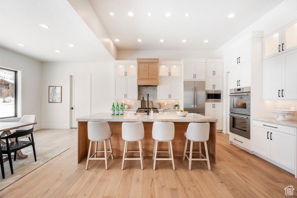 Kitchen featuring light hardwood / wood-style floors, a breakfast bar, white cabinetry, built in appliances, and an island with sink