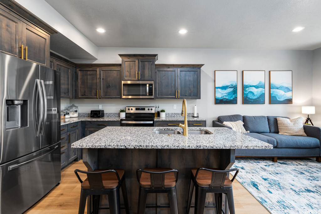 Kitchen with a breakfast bar area, microwave, range oven, refrigerator, light parquet floors, dark brown cabinets, and light stone countertops