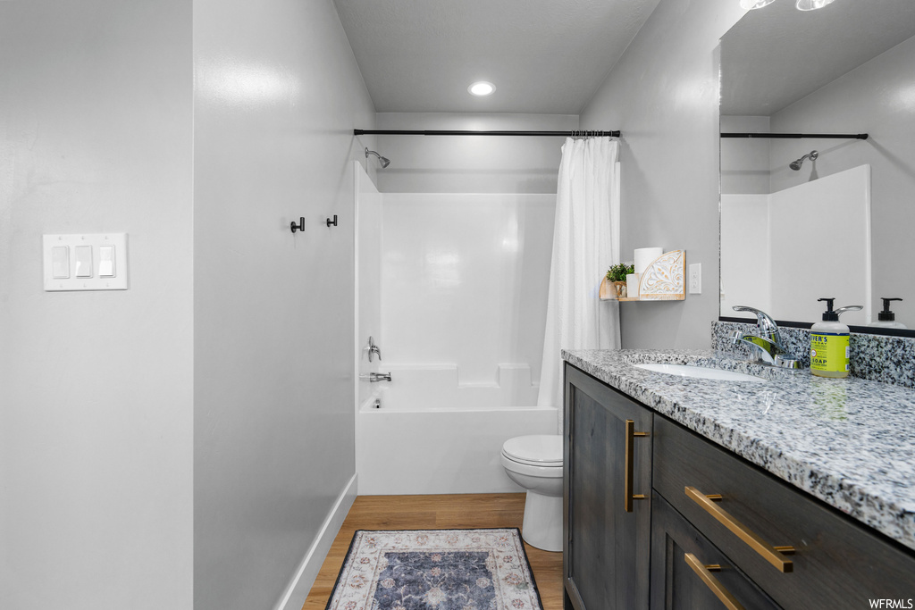 Full bathroom featuring hardwood flooring, mirror, vanity, toilet, shower / tub combination, and shower curtain