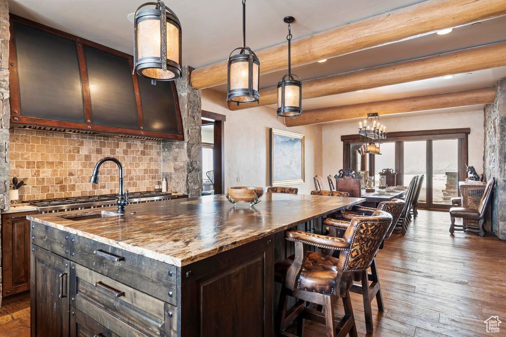 Kitchen featuring light stone counters, tasteful backsplash, dark brown cabinetry, an island with sink, and dark hardwood / wood-style flooring