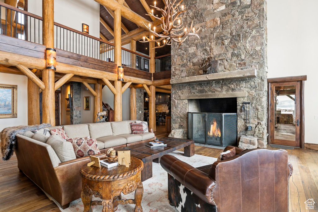 Living room featuring a stone fireplace, a notable chandelier, dark hardwood / wood-style flooring, and a towering ceiling