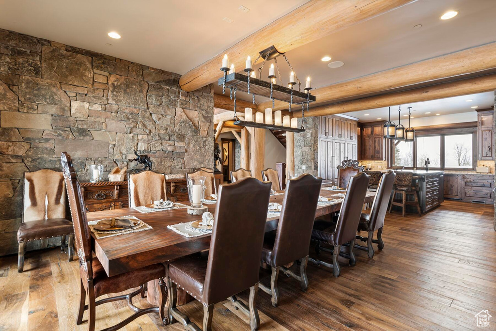Dining area featuring an inviting chandelier, beam ceiling, sink, and dark wood-type flooring