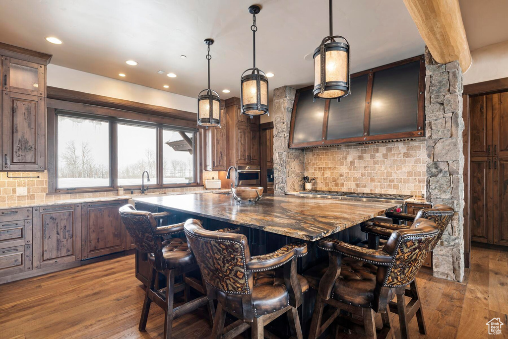 Kitchen with light hardwood / wood-style floors, light stone countertops, an island with sink, a breakfast bar area, and pendant lighting