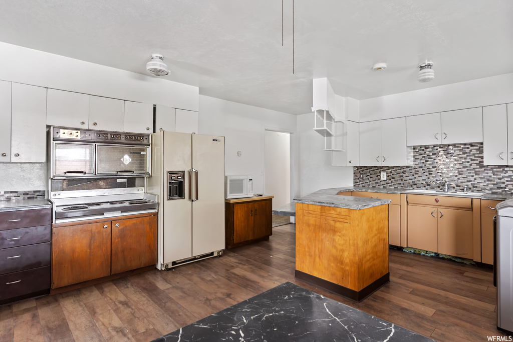 Kitchen featuring dark hardwood floors, backsplash, white cabinets, light countertops, and white appliances