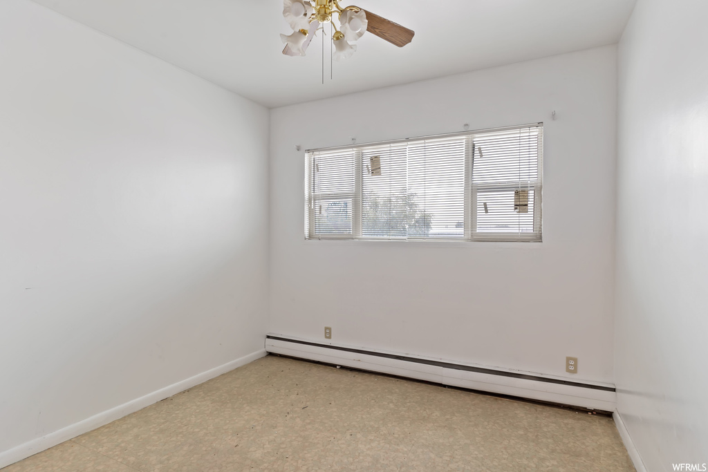 Spare room with a baseboard radiator, ceiling fan, and light tile floors