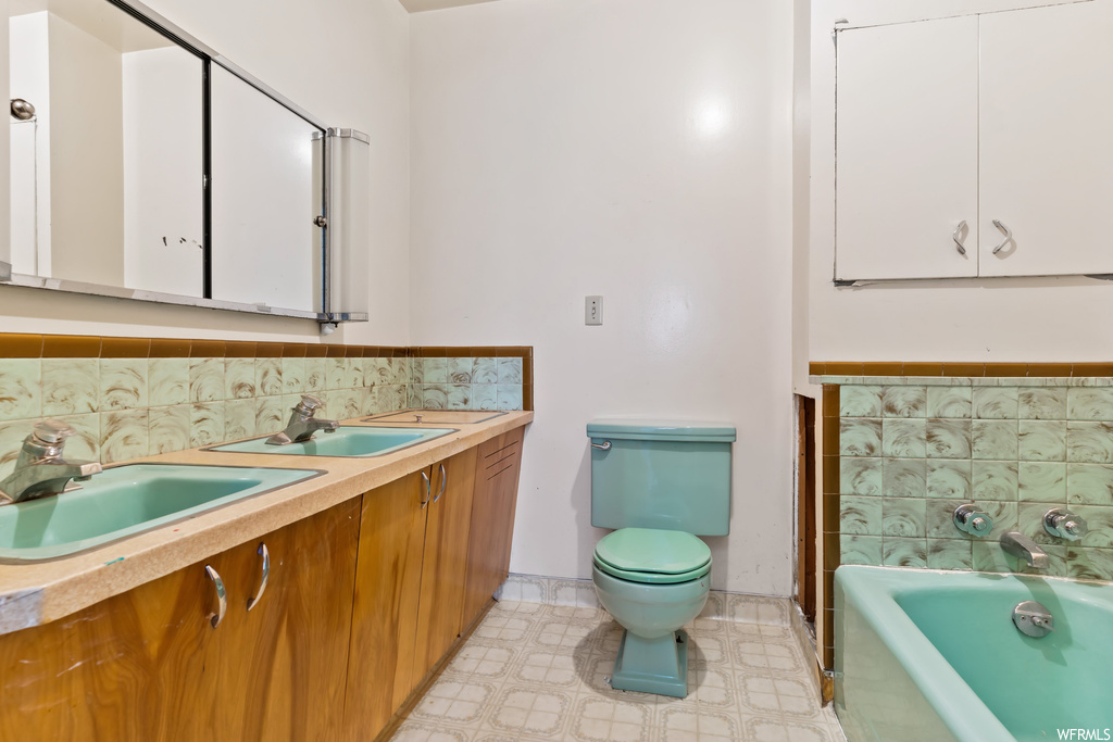 Bathroom featuring a bathing tub, double large vanity, light tile flooring, mirror, and backsplash