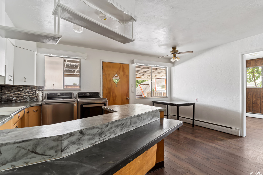 Kitchen with a baseboard radiator, backsplash, hardwood floors, washer / dryer, ceiling fan, and dark countertops