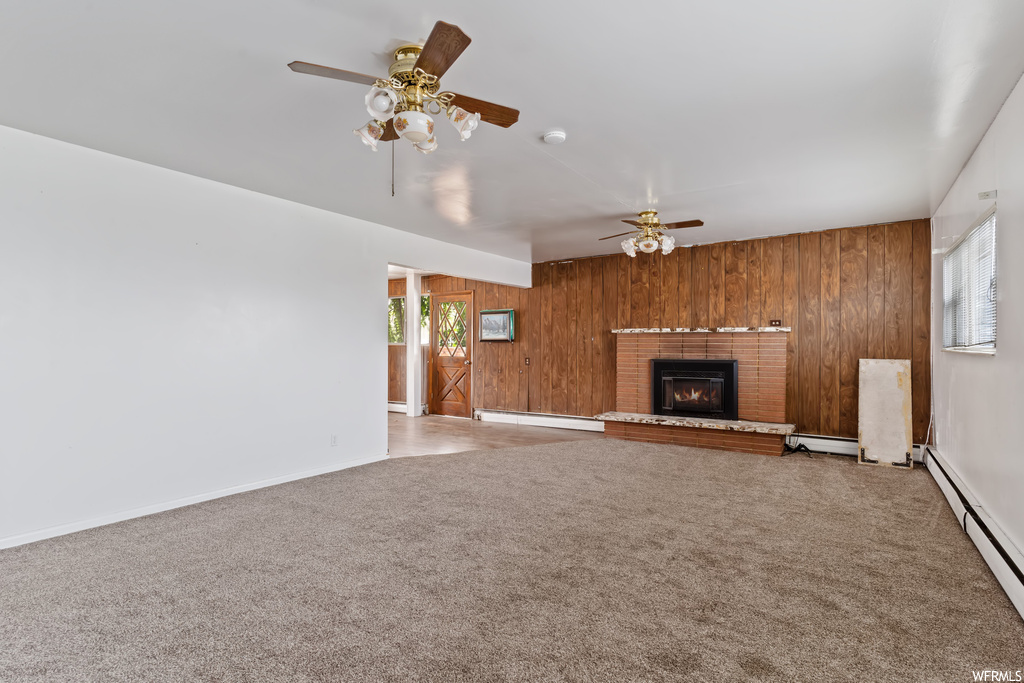 Carpeted living room featuring wooden walls, a fireplace, a baseboard radiator, and ceiling fan