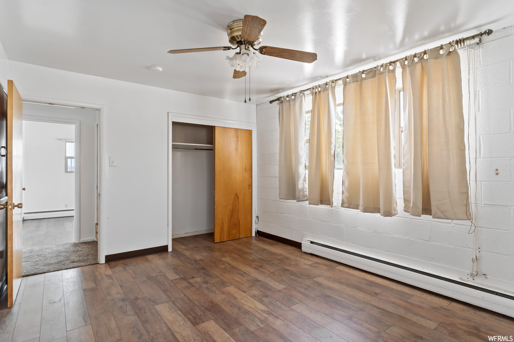 Hardwood floored bedroom with a baseboard heating unit and ceiling fan