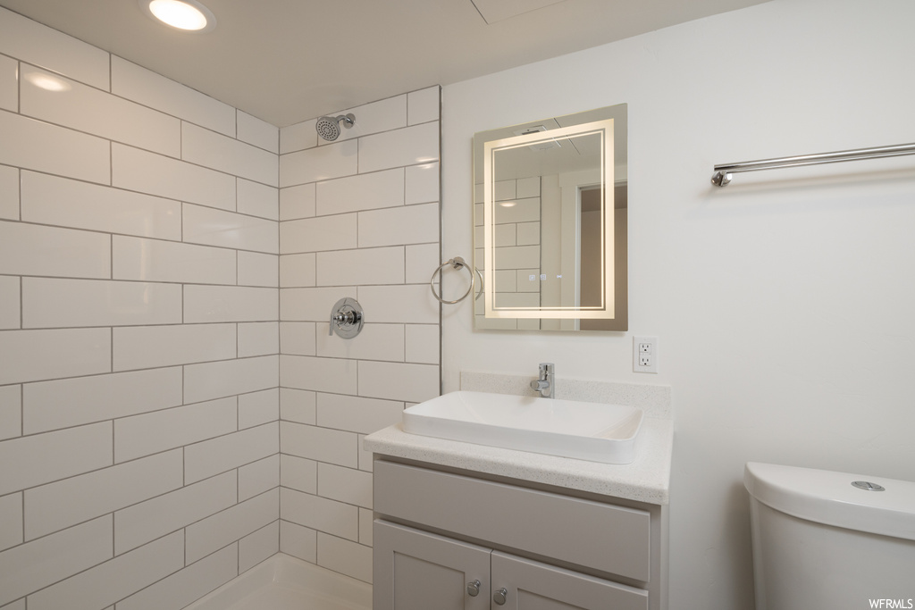 Bathroom with toilet, large vanity, and a tile shower