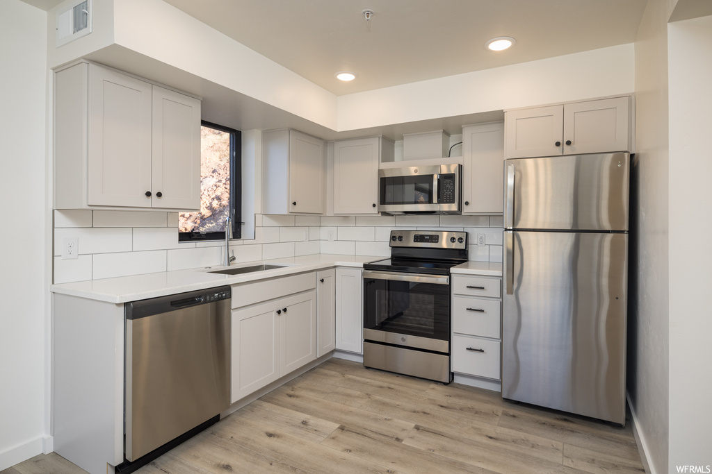 Kitchen with tasteful backsplash, sink, light wood-type flooring, and stainless steel appliances