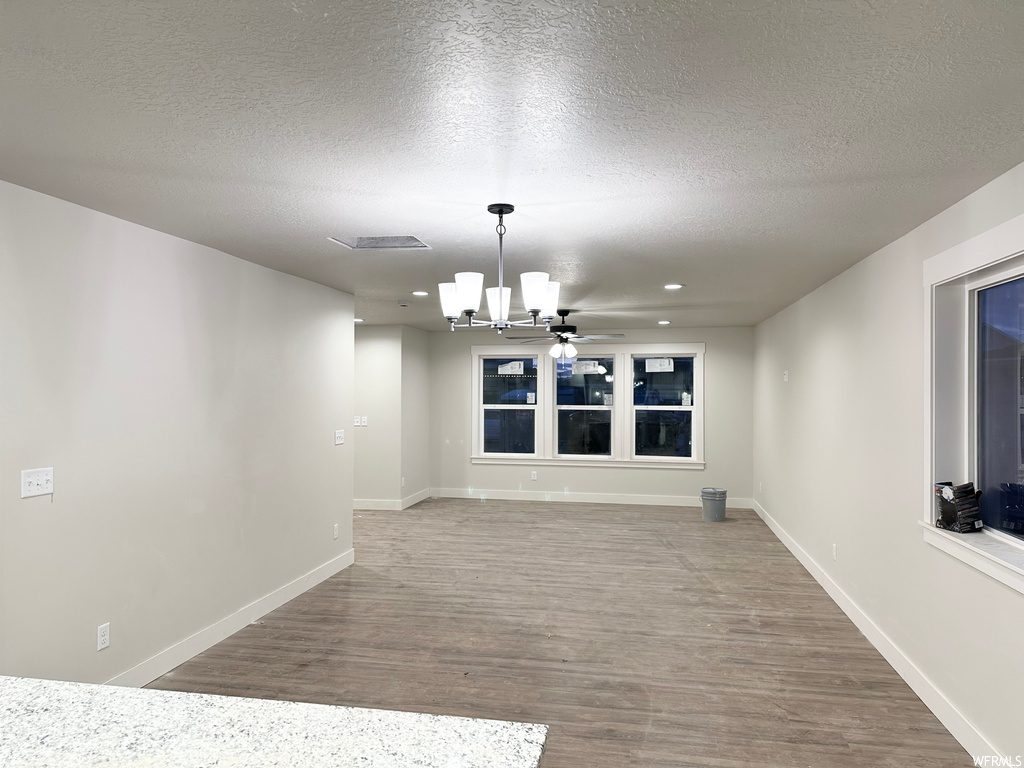 Spare room with a textured ceiling, light hardwood / wood-style floors, and ceiling fan with notable chandelier