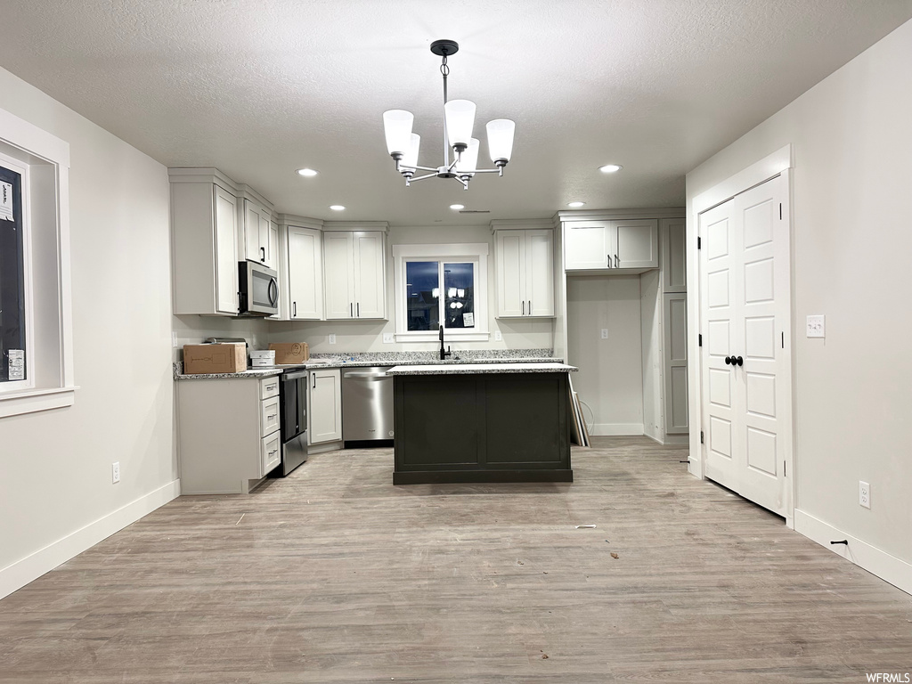 Kitchen with a chandelier, appliances with stainless steel finishes, light hardwood / wood-style floors, a kitchen island, and decorative light fixtures