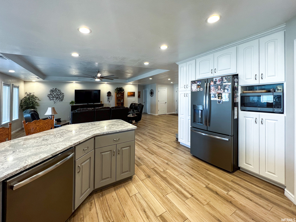 Kitchen with a ceiling fan, TV, dishwasher, microwave, refrigerator, light parquet floors, light stone countertops, and white cabinets