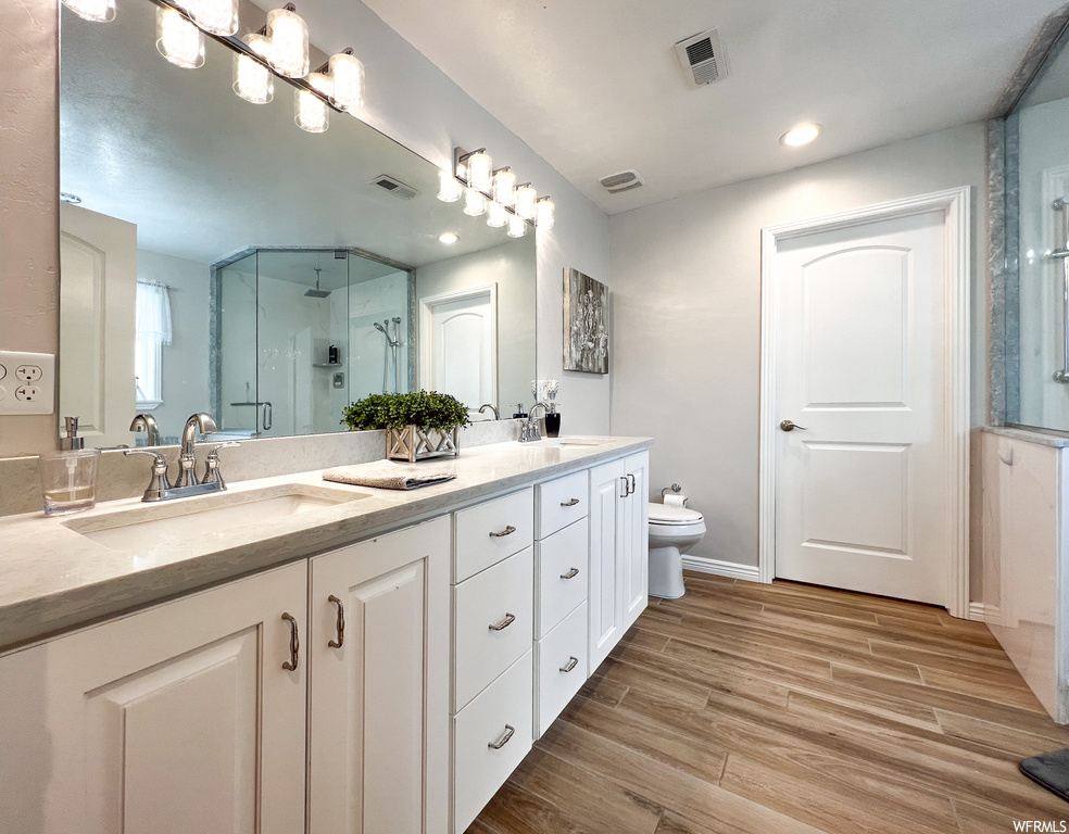 Full bathroom featuring hardwood flooring, his and hers vanity, shower cabin, mirror, and toilet