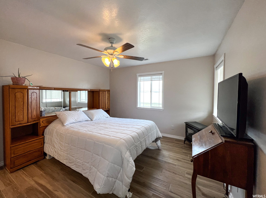 Hardwood floored bedroom featuring a ceiling fan, natural light, and TV