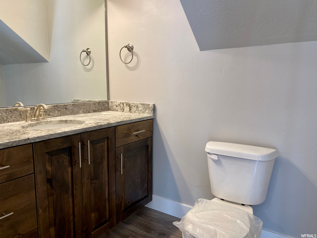 Half bath featuring hardwood floors, toilet, mirror, and vanity