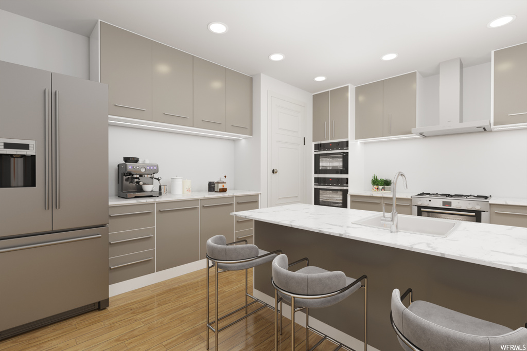 Kitchen featuring a breakfast bar, refrigerator, gas range oven, double oven, fume extractor, light countertops, light hardwood flooring, and white cabinetry