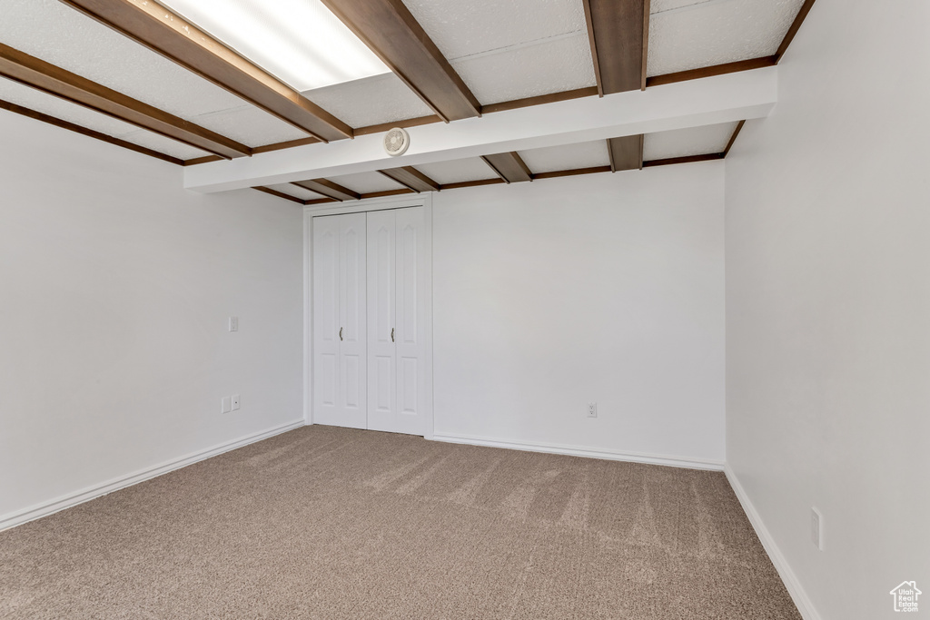 Carpeted empty room featuring beam ceiling