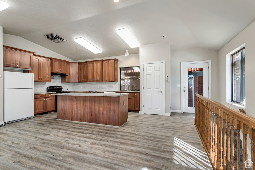 Kitchen featuring white fridge, vaulted ceiling, tasteful backsplash, and light hardwood / wood-style floors