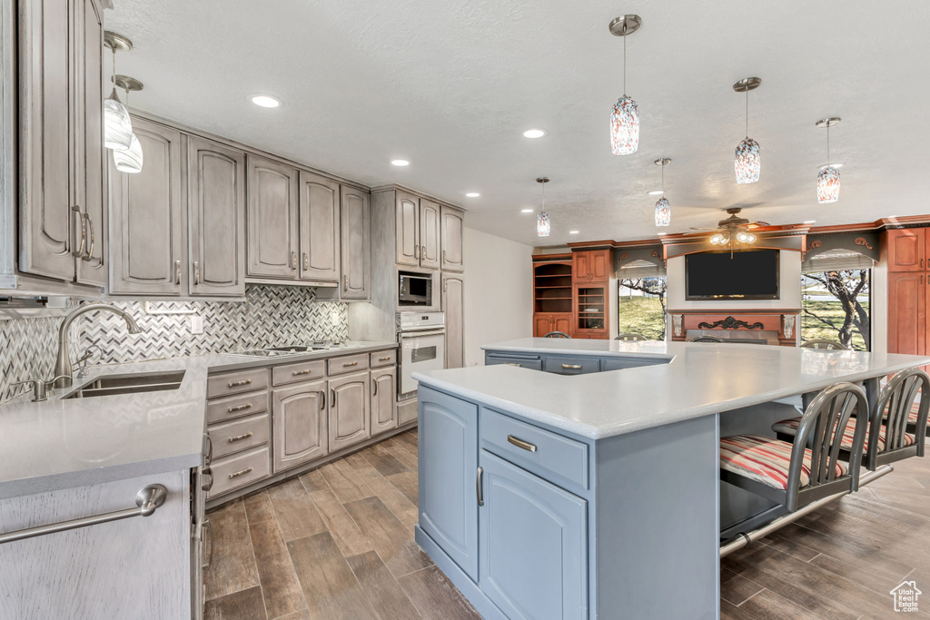 Kitchen featuring ceiling fan, pendant lighting, appliances with stainless steel finishes, a kitchen island, and wood-type flooring