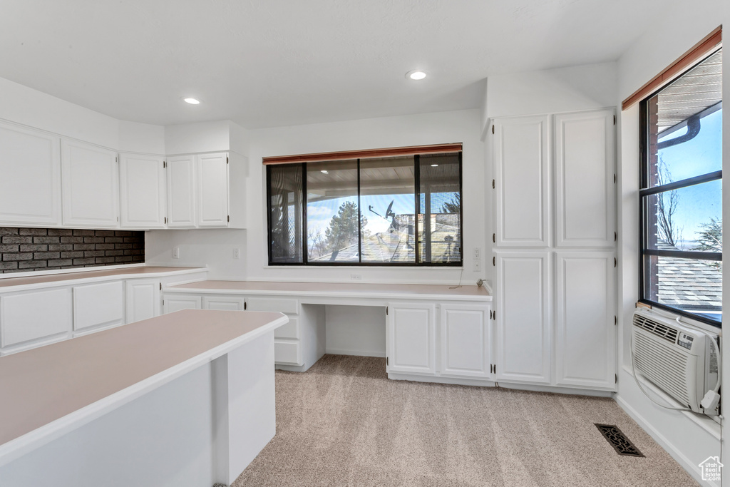 Kitchen with tasteful backsplash, white cabinetry, and light carpet