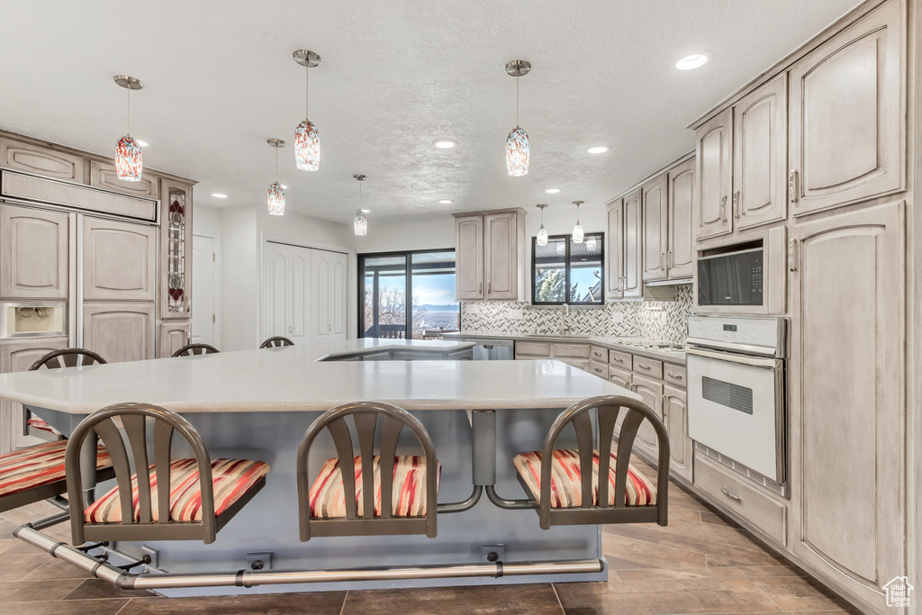 Kitchen with built in appliances, a breakfast bar, decorative light fixtures, and a center island with sink
