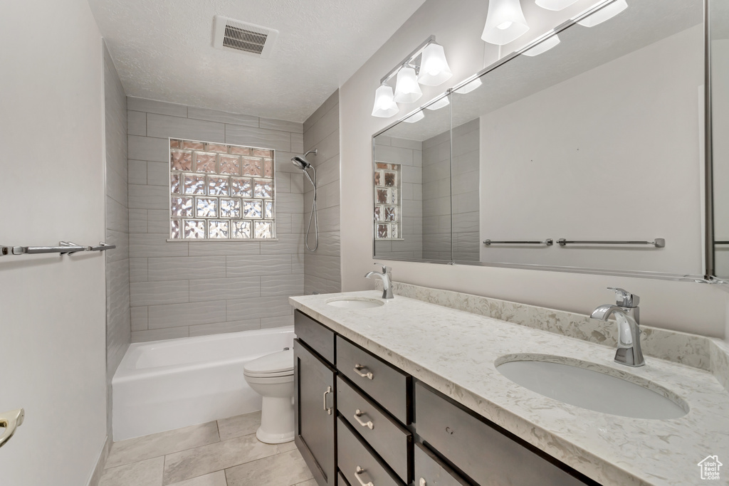 Full bathroom with tiled shower / bath combo, a textured ceiling, dual bowl vanity, toilet, and tile floors