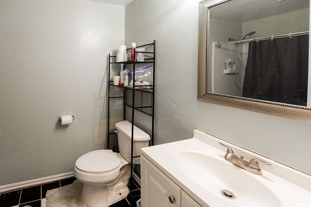 Bathroom with toilet, shower curtain, mirror, and vanity with extensive cabinet space