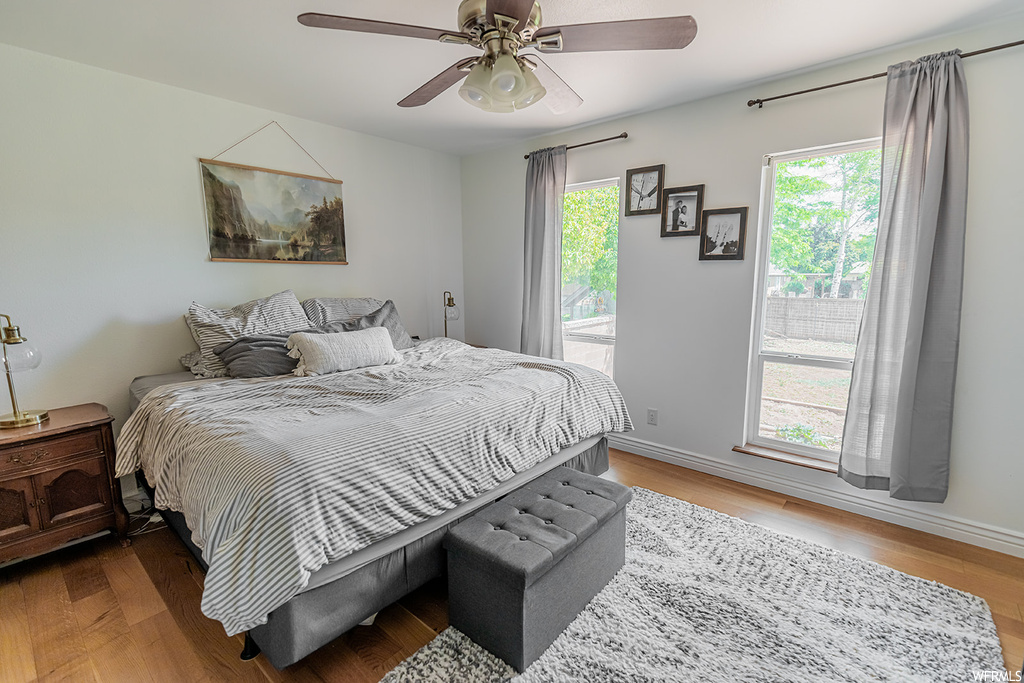 Hardwood floored bedroom with a ceiling fan and natural light