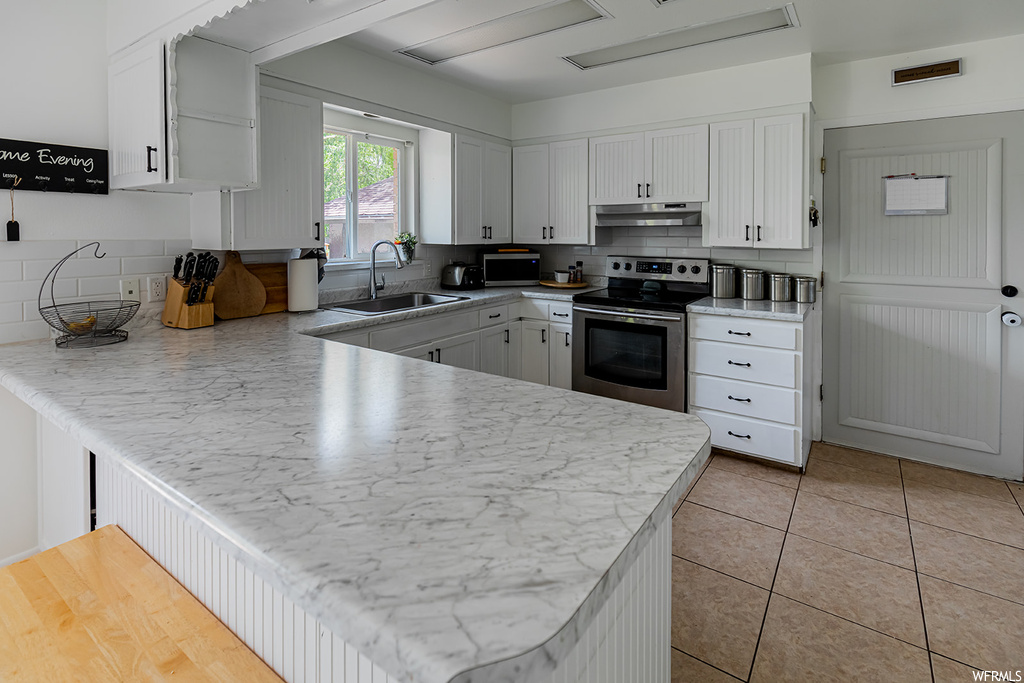 Kitchen featuring natural light, electric range oven, stainless steel finishes, fume extractor, white cabinets, light countertops, and light flooring