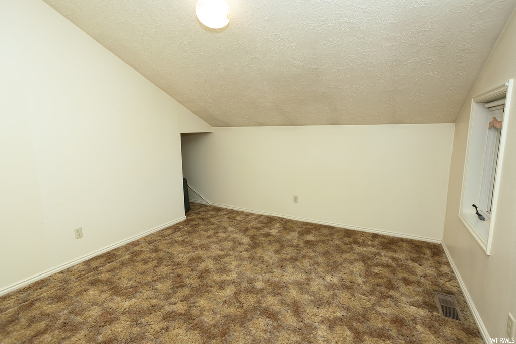 Bonus room with dark carpet, vaulted ceiling, and a textured ceiling