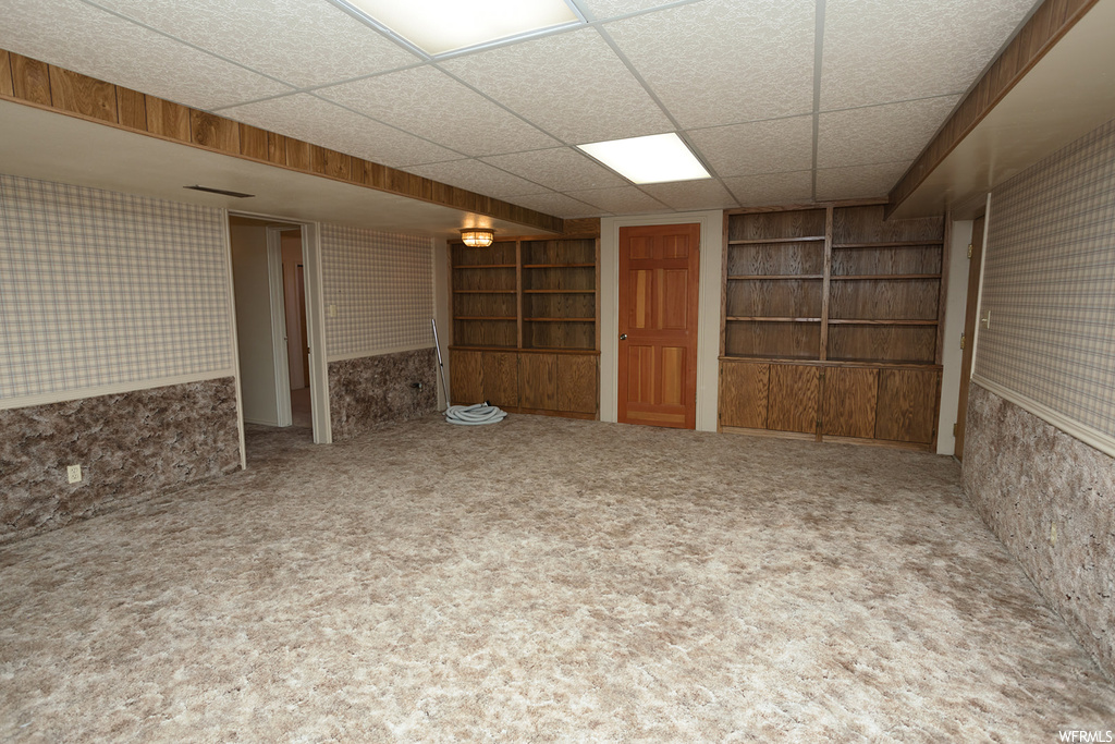 Basement featuring built in shelves, carpet flooring, and a drop ceiling