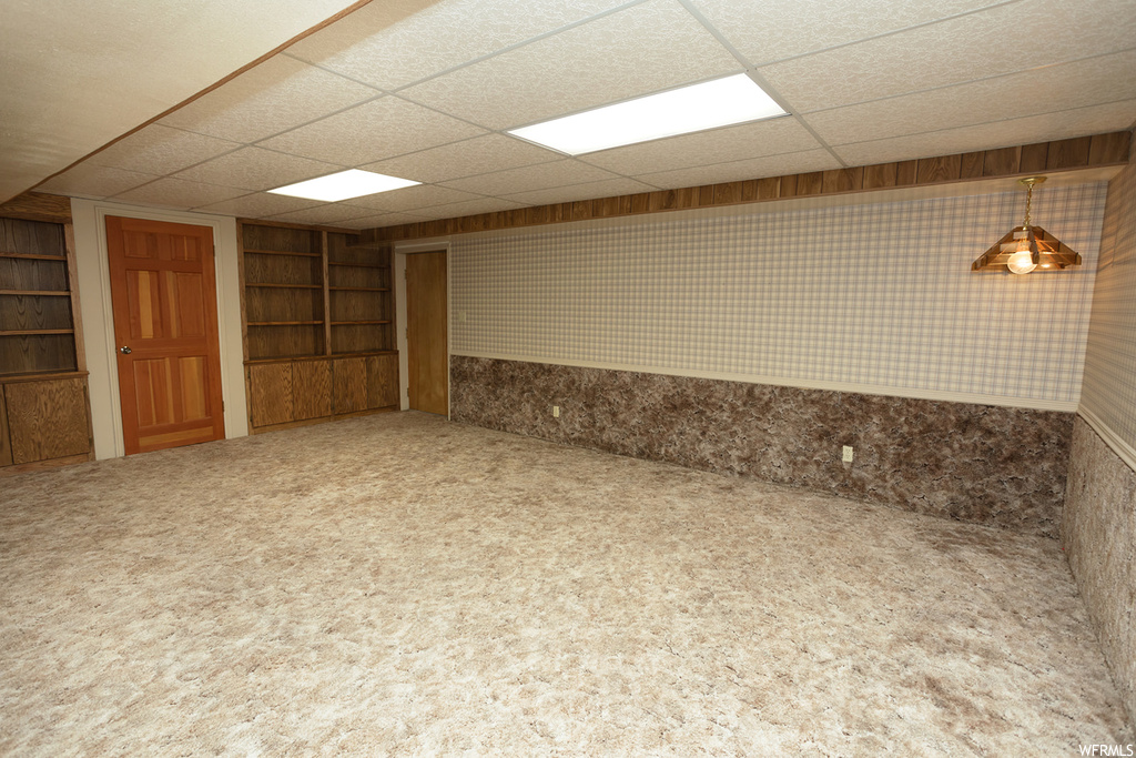 Basement with built in shelves, a drop ceiling, and carpet flooring