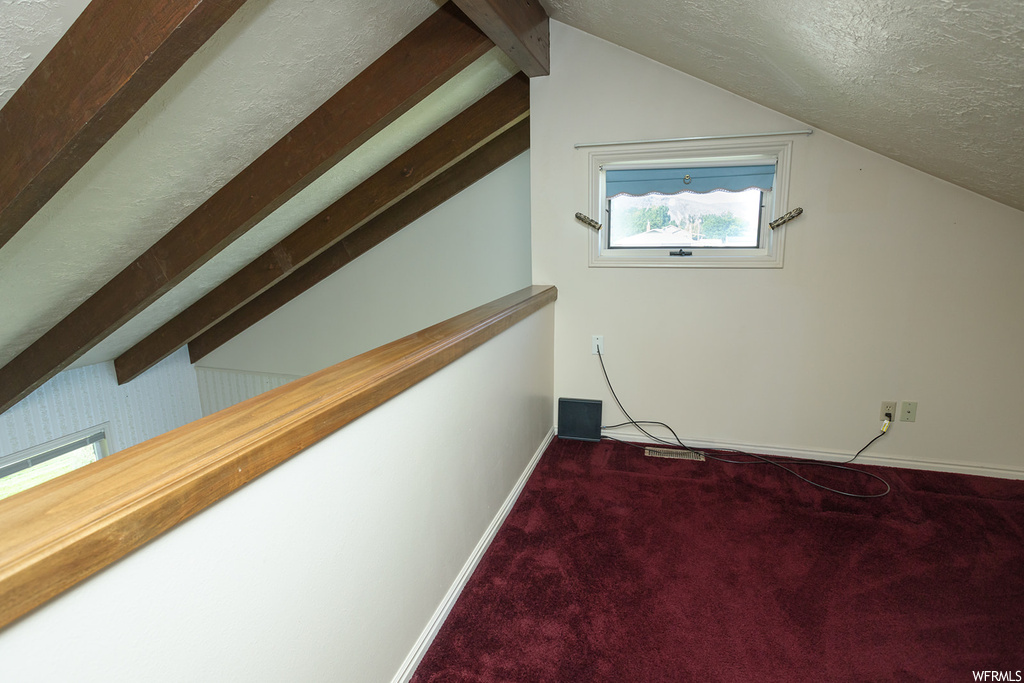 Bonus room with dark carpet, lofted ceiling, and a textured ceiling
