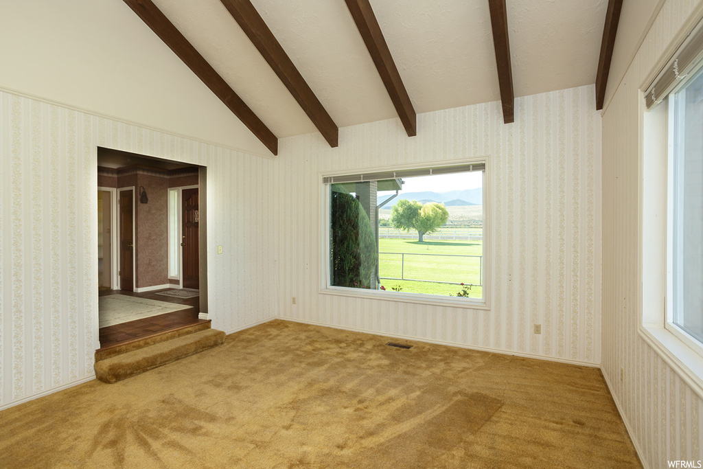 Unfurnished room featuring light carpet and lofted ceiling with beams