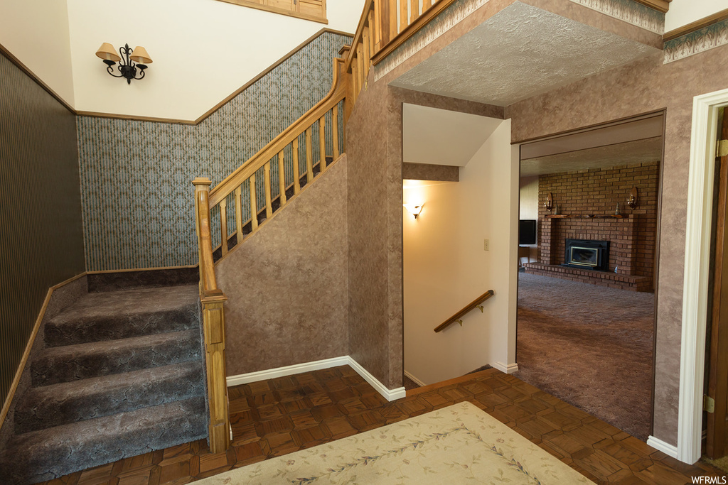 Staircase featuring brick wall, dark carpet, and a textured ceiling