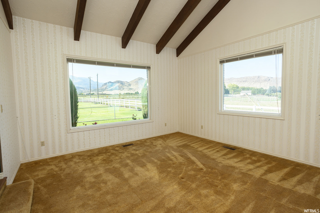 Carpeted empty room featuring vaulted ceiling with beams and plenty of natural light