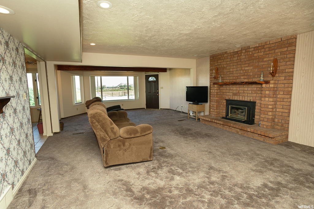 Living room featuring a textured ceiling, a fireplace, brick wall, and light carpet