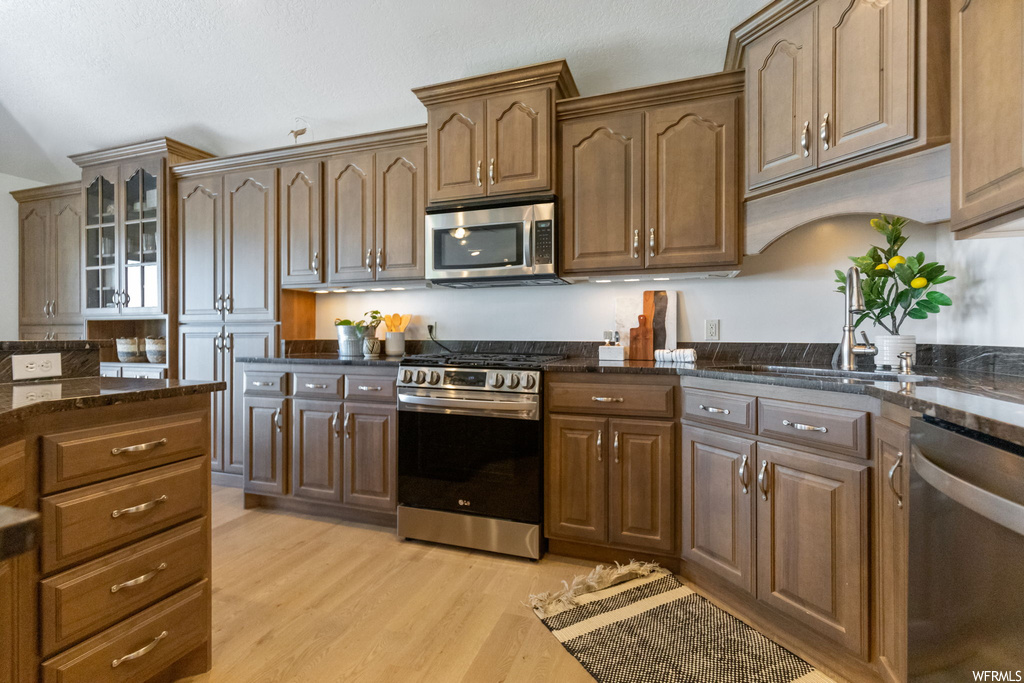 Kitchen with dark countertops, appliances with stainless steel finishes, light hardwood flooring, and brown cabinets