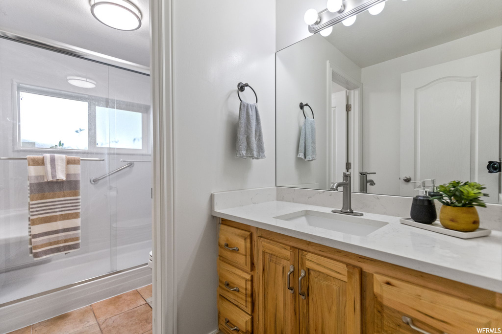 Bathroom with mirror, large vanity, a shower with door, and light tile floors