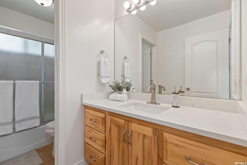 Full bathroom with mirror, vanity, bath / shower combo with glass door, and light tile flooring
