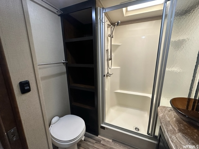 Full bathroom featuring hardwood floors, shower with glass door, toilet, and vanity