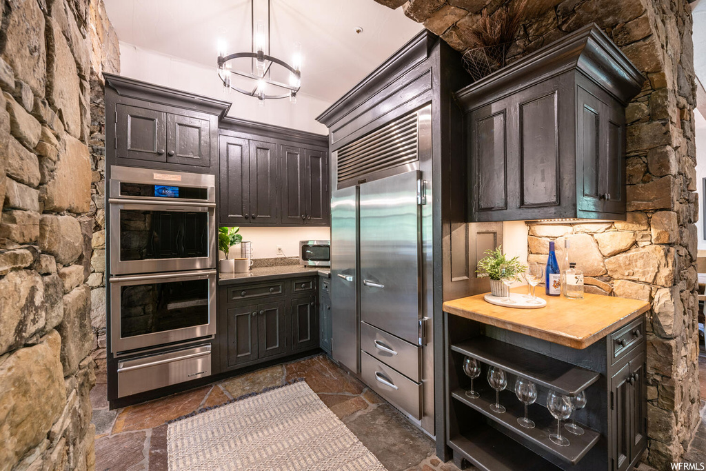 Kitchen featuring refrigerator, double oven, light countertops, dark brown cabinetry, and dark flooring