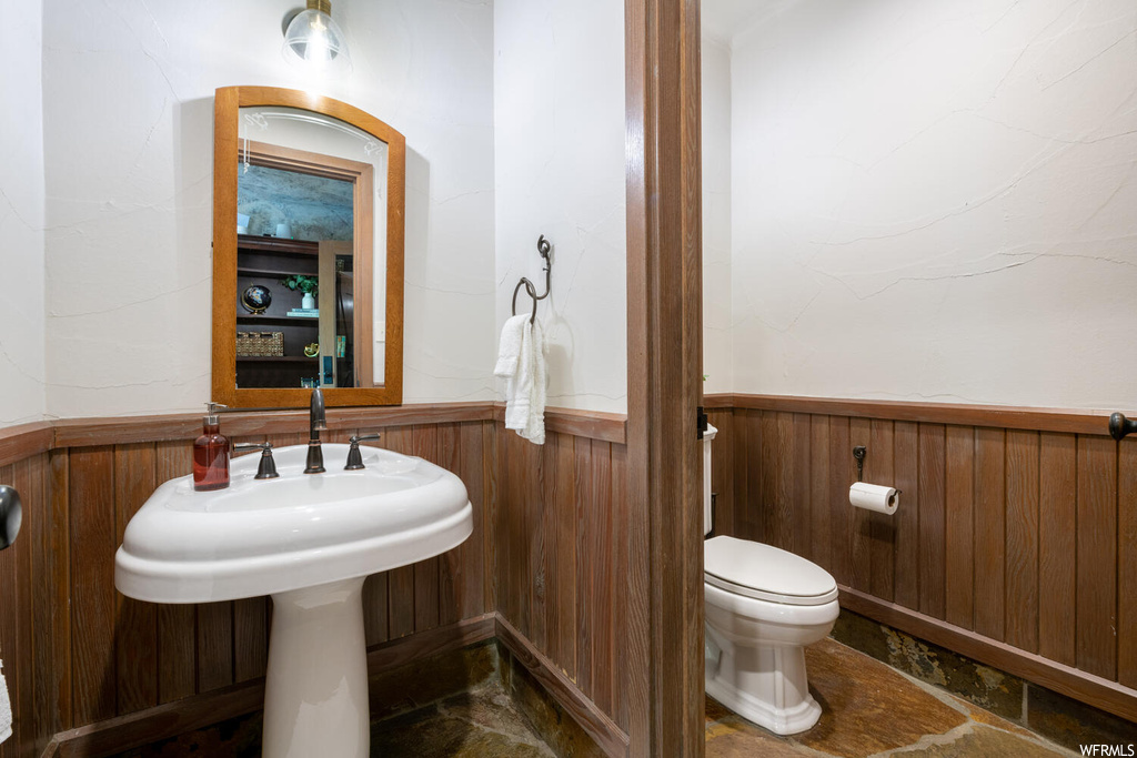 Half bathroom featuring tile flooring, toilet, mirror, and washbasin