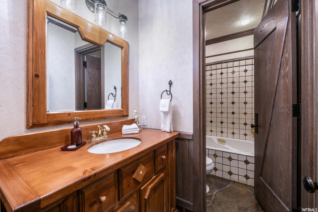 Full bathroom with tile floors, toilet, mirror, vanity, and tub / shower combination