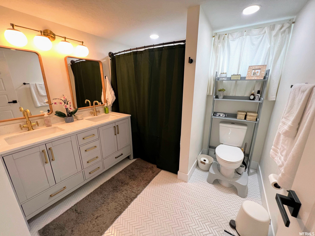 Bathroom with tile floors, toilet, shower curtain, mirror, and dual bowl vanity